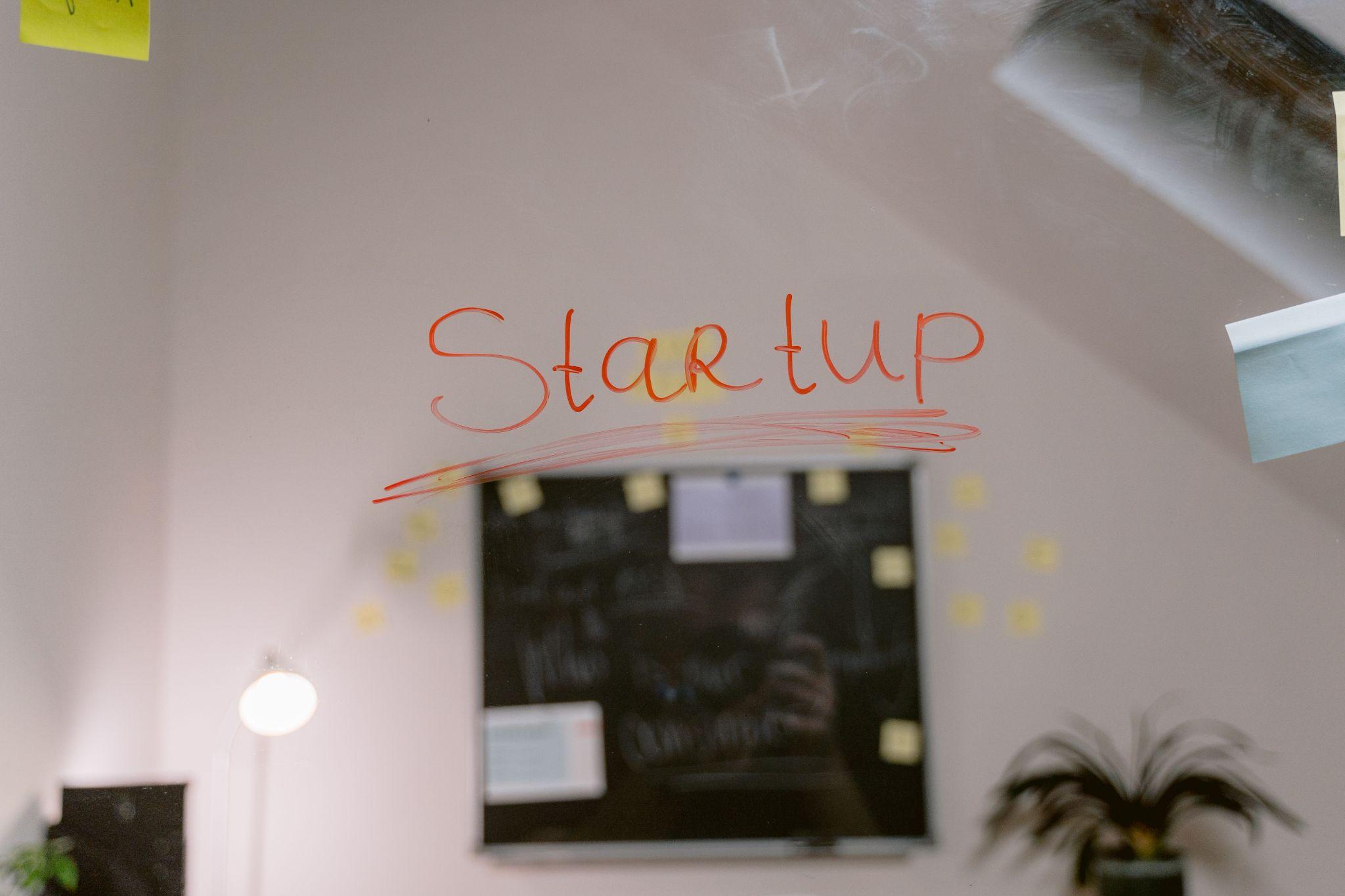 The word Startup handwritten in red marker on a glass wall in a small office, illustrating how a startup can build a professional brand identity on a budget